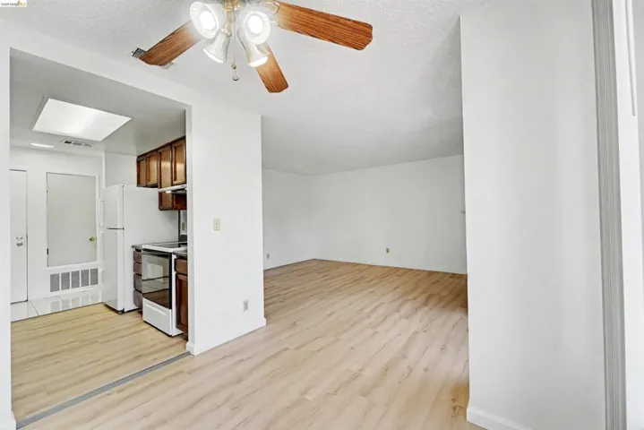 Open-concept living space featuring wood-finish flooring throughout, a kitchen with wood cabinetry and a white appliance suite, and a ceiling fan with integrated lighting