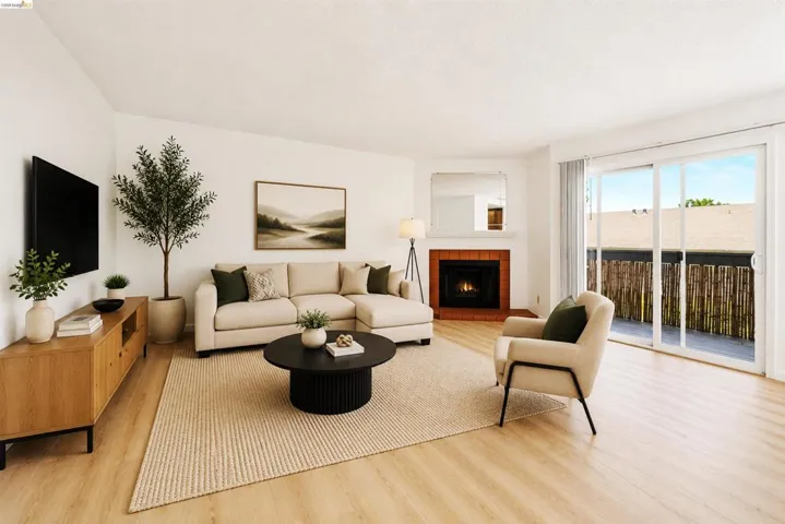 Bright open living space featuring light wood-finish flooring, a corner fireplace with brick surround, and a large sliding glass door