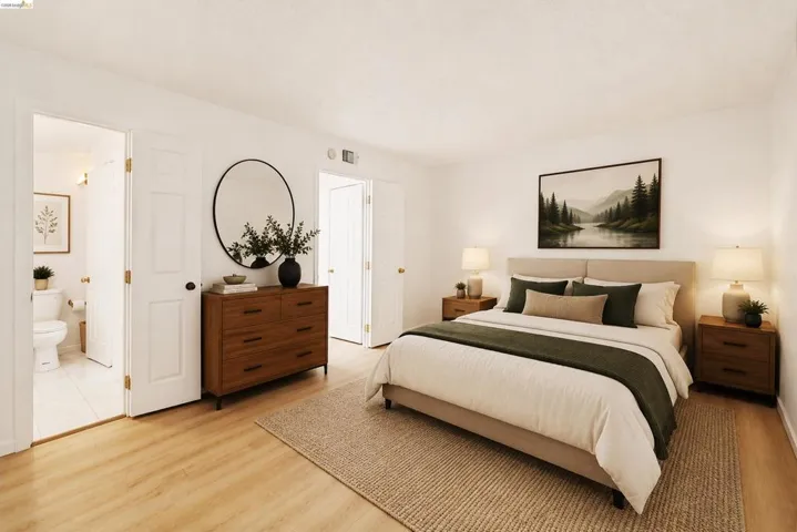 Well-lit bedroom with light wood-finish flooring, white walls, and two white paneled doors