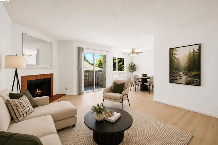 Open-concept living space featuring wood-finish flooring, a fireplace with a terra cotta tile surround, and a glass sliding door opening to a private balcony