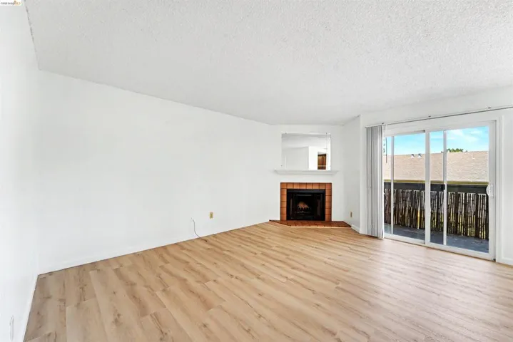 Living area featuring wood-finish flooring, a corner fireplace with brick surround, white mantel, and a mirrored accent