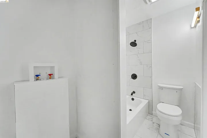 Bathroom featuring a white bathtub with a tile surround, a white toilet, and tile flooring