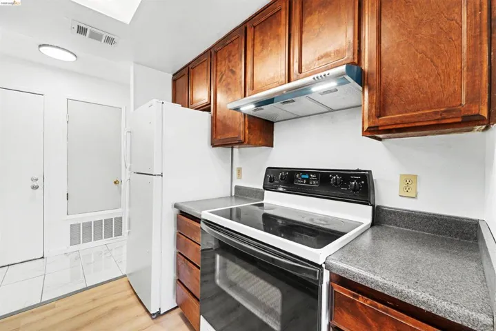 Kitchen featuring wood cabinetry, dark countertops, a black electric range with a built-in oven, and a range hood with integrated lighting
