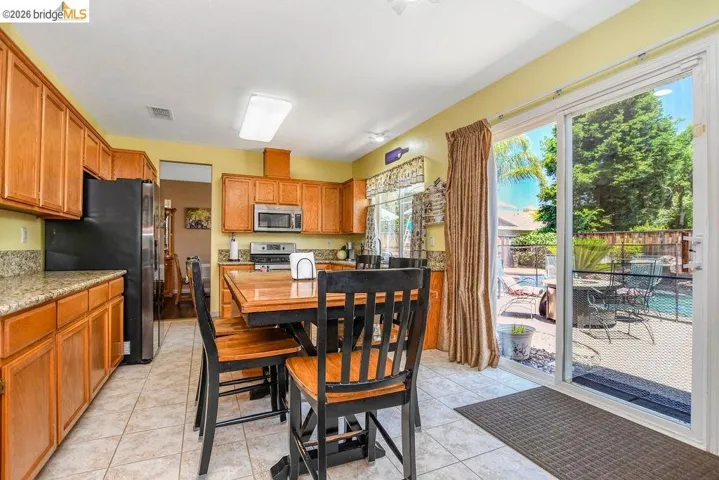 Kitchen featuring wood finish cabinetry, stainless steel appliances, light tile patterned flooring, and light stone counters