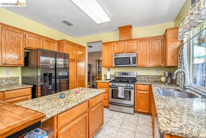 Kitchen featuring stainless steel appliances, light stone counters, wood finish cabinetry, and light tile patterned floors