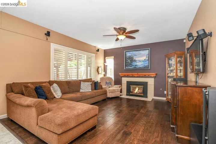 Living area with dark wood-style flooring, ceiling fan, and a tiled fireplace