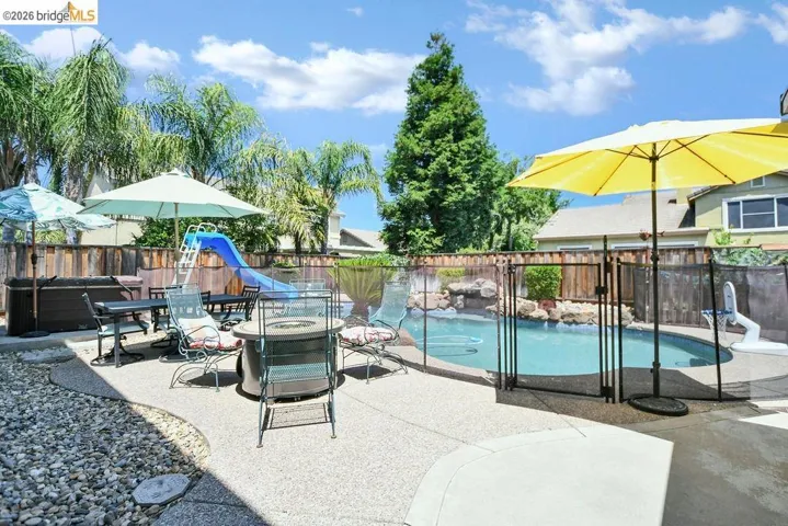 View of pool with patio surround, a fenced backyard, outdoor dining area, and a water slide