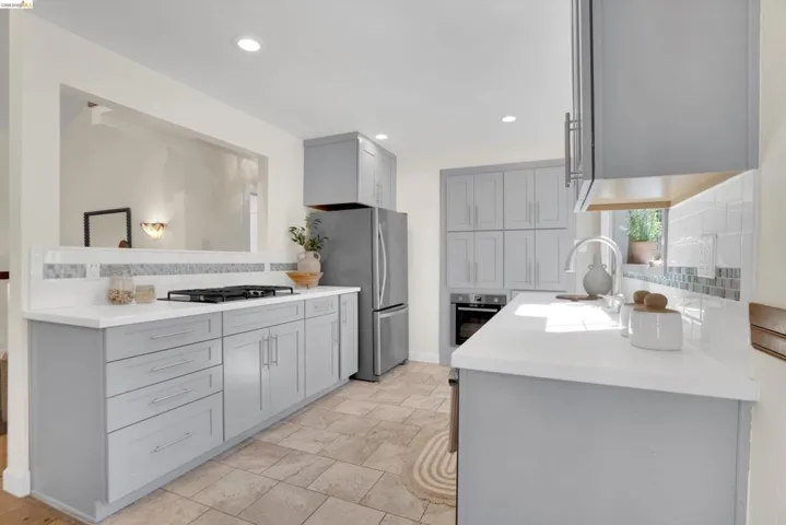 Modern kitchen featuring light gray cabinetry, white countertops, tile flooring, and a stainless steel refrigerator
