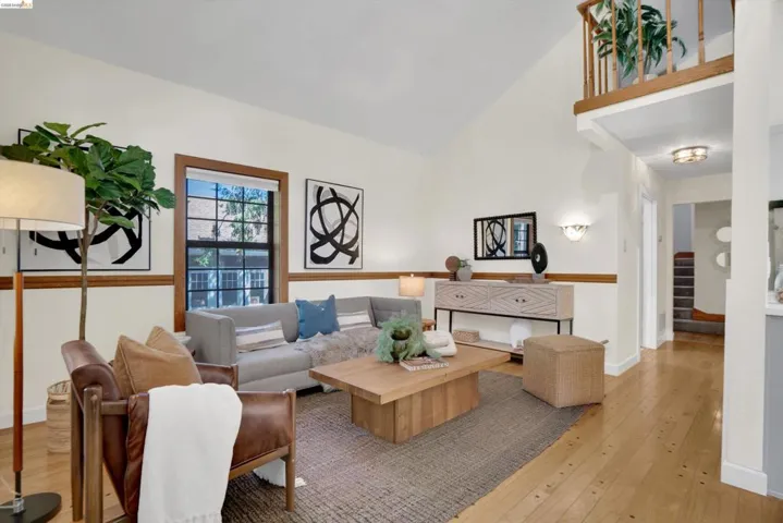 Living area featuring vaulted ceilings, wood-finish flooring, a prominent window with wood trim, and a second-story interior balcony with wood railing