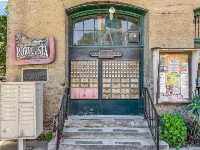 Historic building facade featuring a prominent arched entryway with transom windows, a multi-unit mailbox system, a bulletin board enclosure, and a decorative outdoor sign