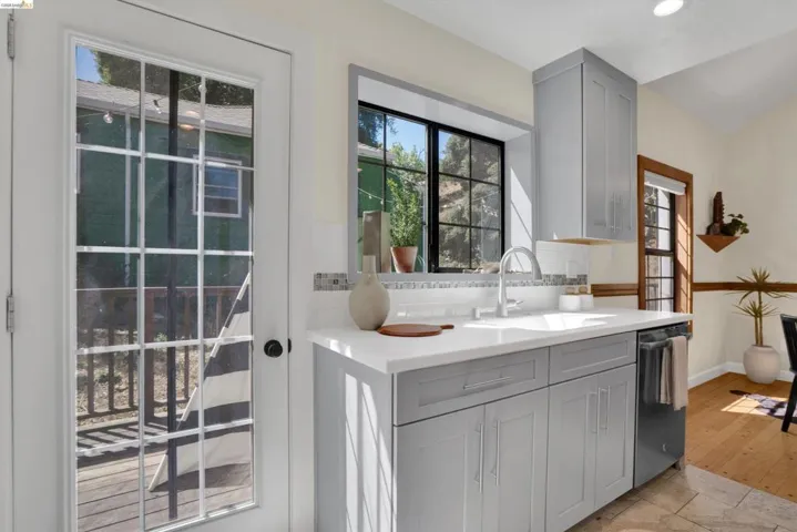 Modern kitchen featuring light gray cabinetry with brushed nickel hardware, white countertop, and a stainless steel dishwasher