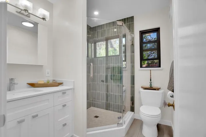 Bathroom featuring a glass-enclosed shower with vertical tile, a single vanity with stone countertop, and wood-finish flooring