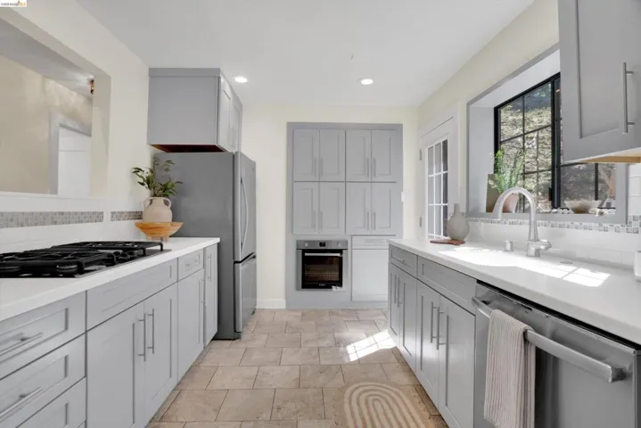 Kitchen featuring extensive gray cabinetry, light countertops, stainless steel appliances, tile flooring, and a window above the sink