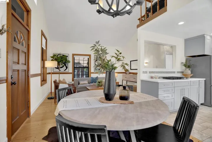 Vaulted ceiling with an overhead chandelier, wood-finish flooring, half-lite wood entry door, light gray kitchen cabinetry, and white countertops