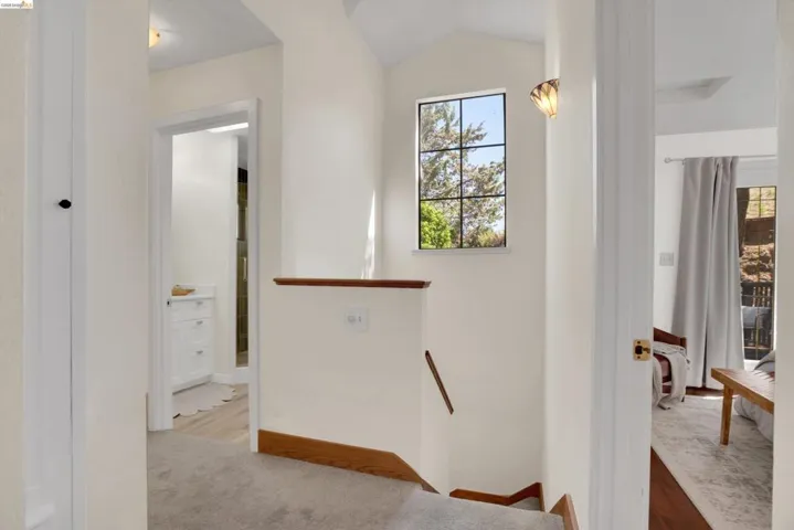Upper-level hallway featuring a grid-pattern window, vaulted ceiling, neutral wall tones, and wood-finish trim accents