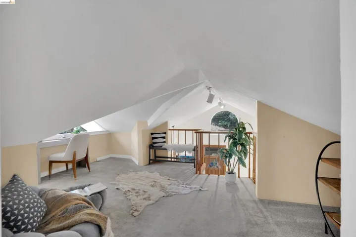 Vaulted ceiling loft space featuring light carpet flooring, a built-in dormer desk, and a decorative wood railing