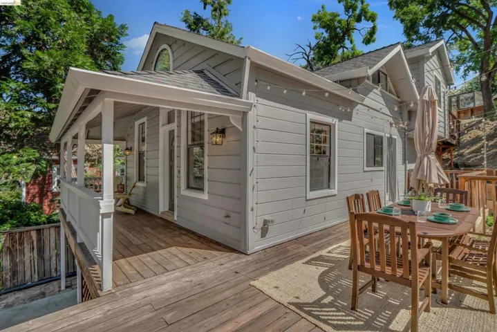 Expansive multi-level wood deck featuring a covered porch with white railing, exterior wall sconces, and string lighting