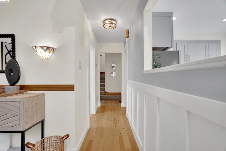 Hardwood flooring extending through a hallway, featuring a decorative ceiling light fixture and a wall-mounted sconce