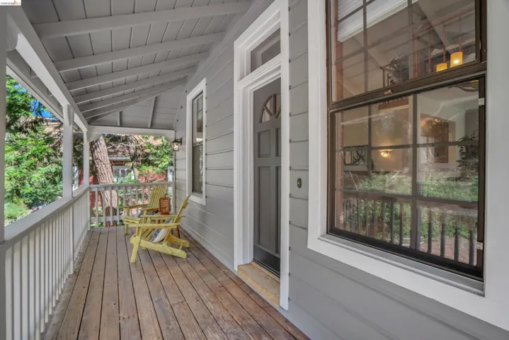 Covered front porch featuring wood-finish flooring, white railing, grey siding, a dark entry door with arch detail, and a large window with white trim