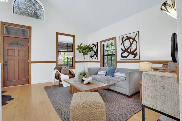 Vaulted ceiling living space with wood-finish flooring, a paneled wood entry door with an arched transom, and additional windows featuring wood trim