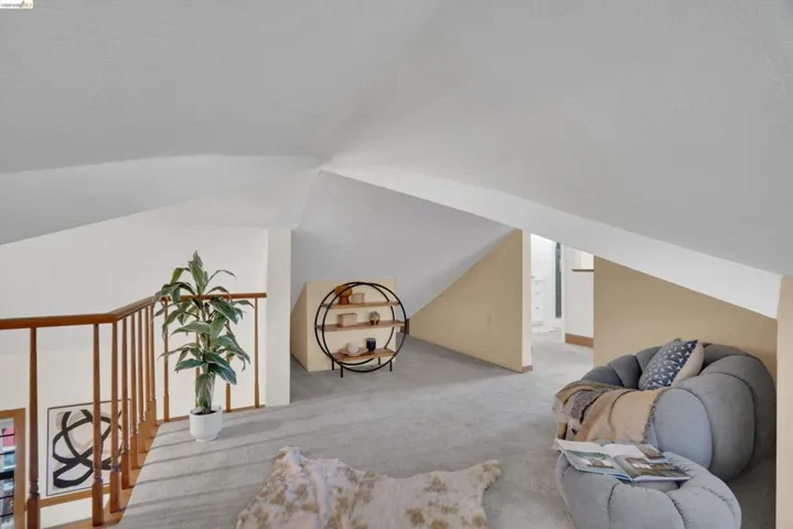 Loft space with sloped ceilings and light gray carpeting