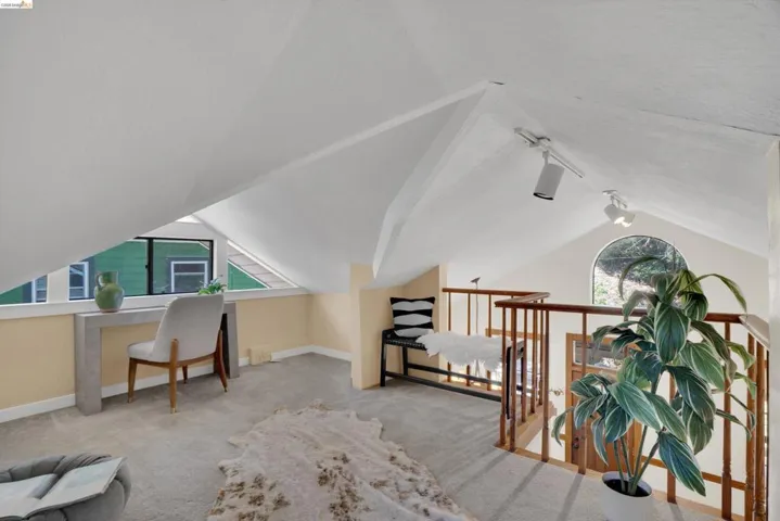 Open loft space featuring vaulted ceilings, track lighting, and soft carpet flooring