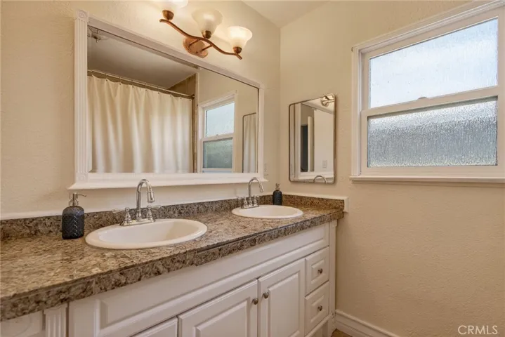 Hallway bathroom with dual sinks and a spa tub with shower.