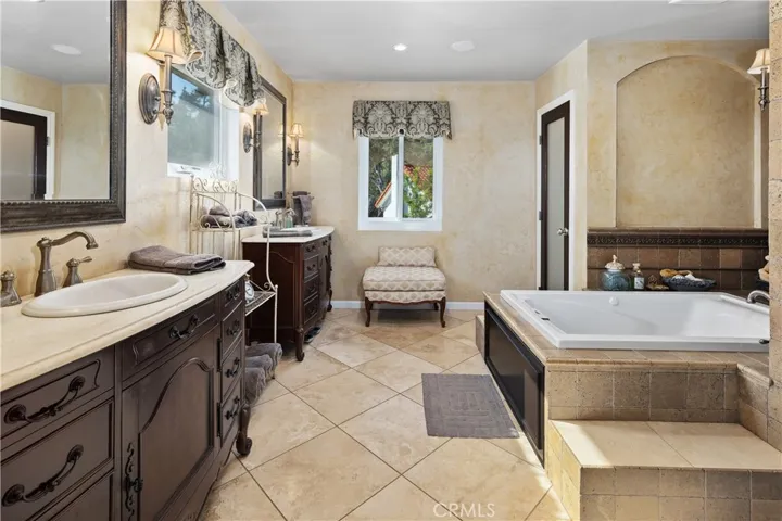 Another view of the primary bathroom with stone flooring and counters.  Custom finished walls adds to the French Provincial theme