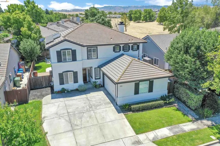 Two-story stucco residence featuring a tile roof, dark shutters, and a concrete driveway