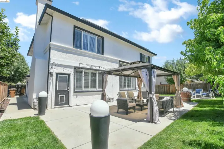 Spacious backyard featuring a concrete patio, lush green lawn, private wood fencing, and mature trees