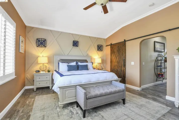 Accent wall with dimensional paneling, wood-finish flooring, vaulted ceiling, white window shutters, and a dark wood barn door