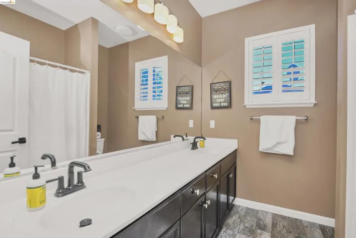 Bathroom featuring a dual vanity with white countertops, dark wood-finish cabinetry, and brushed nickel hardware