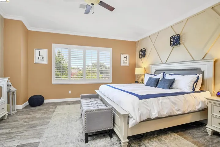 Bedroom featuring a geometrically paneled accent wall, crown molding, and wood-finish flooring