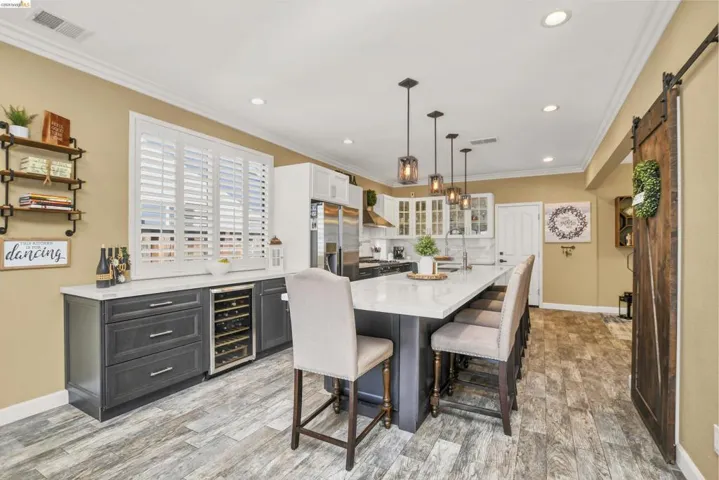Kitchen featuring a large central island with seating, pendant lighting, stainless steel appliances, a built-in wine refrigerator, and wood-finish flooring