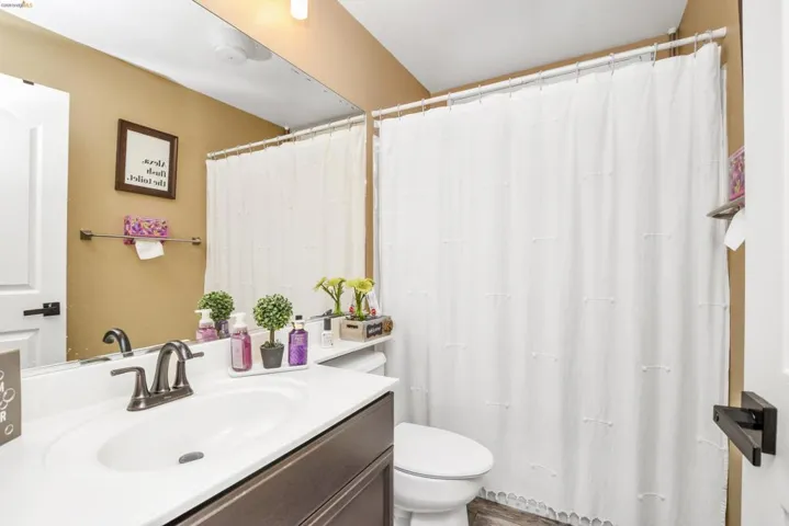 Bathroom featuring a white vanity with an integrated sink, dark bronze-finish fixtures, a full-width mirror, a white toilet, and a shower with a white curtain