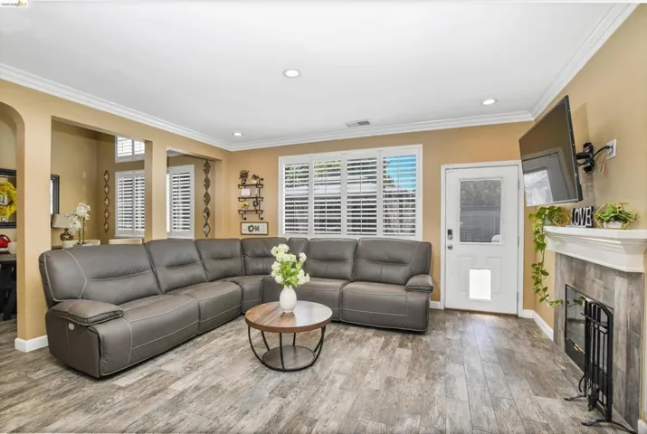 Living area featuring wood-finish flooring, a fireplace with a tiled surround and white mantel, and crown molding