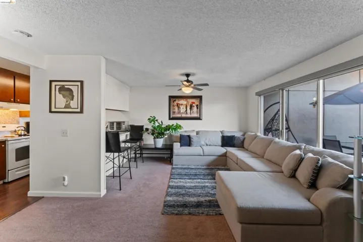 Living room featuring a textured ceiling, dark carpet, and ceiling fan