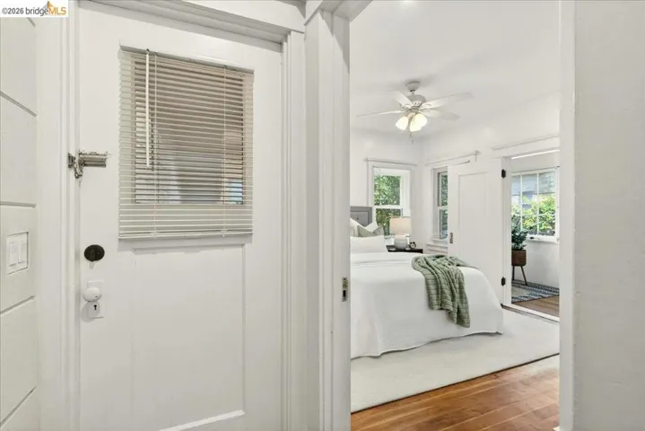 Bright interior space featuring a white painted door with an integrated blind, wood-finish flooring, a ceiling fan with integrated lighting, and multiple windows allowing natural light