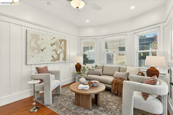 Bright living area featuring wood-finish flooring, white board and batten wall paneling, and a contemporary ceiling fan with integrated lighting