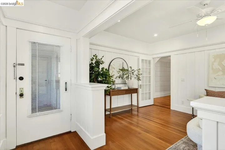 Inviting entry space featuring warm wood-finish flooring, white shiplap wall paneling, a ceiling fan with integrated lighting, and French doors leading to an interior room