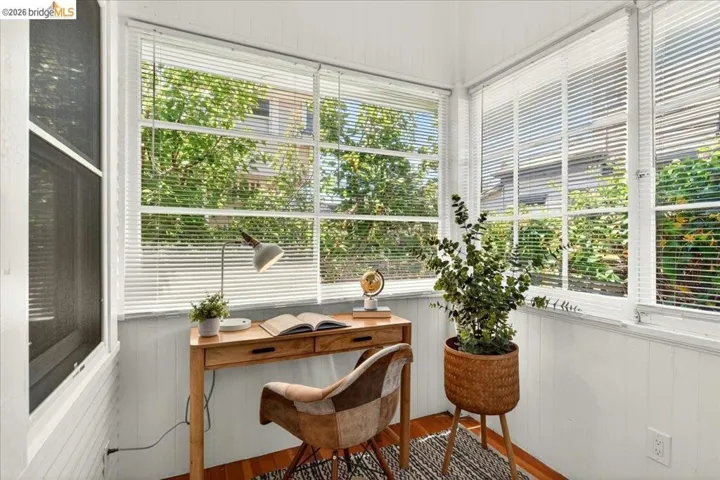Sunroom featuring multiple large windows with white blinds, white paneled walls, and wood-finish flooring