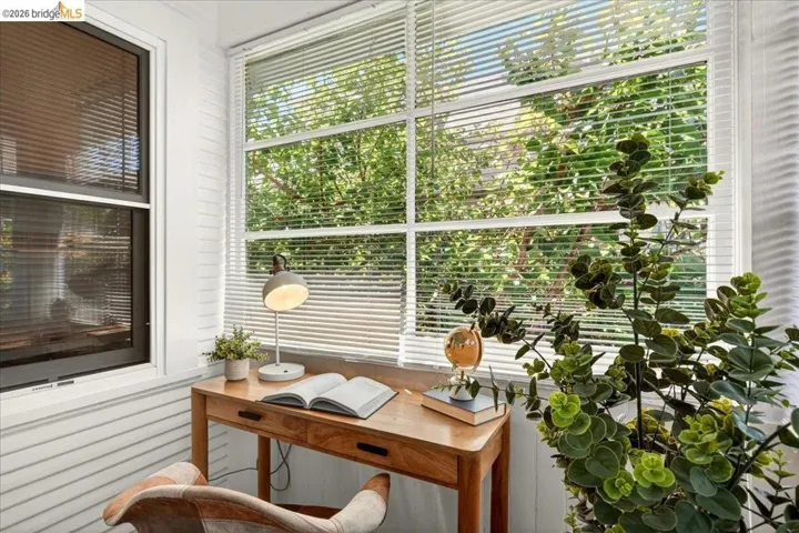 Bright sunroom featuring multiple windows with horizontal blinds, shiplap wall paneling, and a natural wood-finish desk with drawers