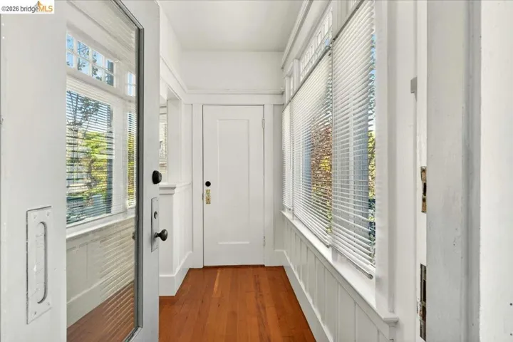 Sunroom with wood-finish flooring, white paneled wainscoting, multiple windows with blinds, transom windows, and white trim