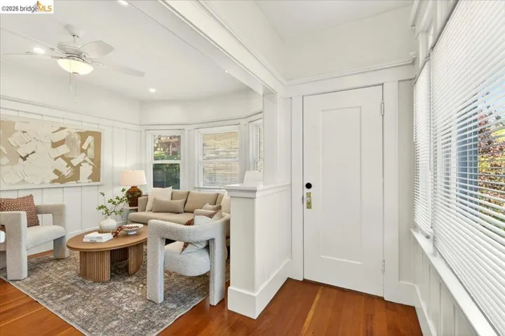 Living room featuring rich wood-finish flooring, white paneled walls, and a multi-light ceiling fan