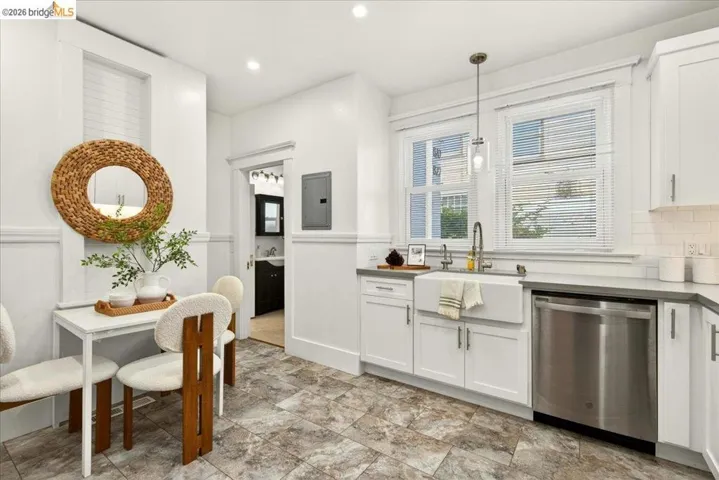 Contemporary kitchen featuring white cabinetry, a farmhouse-style sink with a gooseneck faucet, stainless steel dishwasher, and a tile backsplash