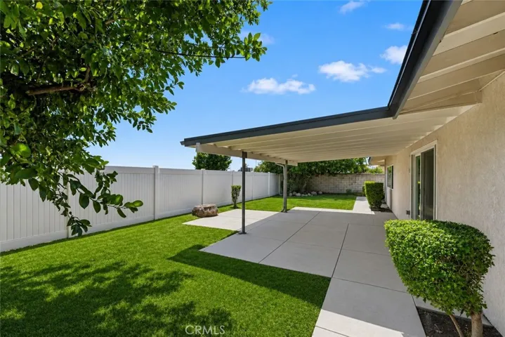 Expansive covered patio overlooks a spacious backyard with mature shade trees and ample room for outdoor entertaining.
