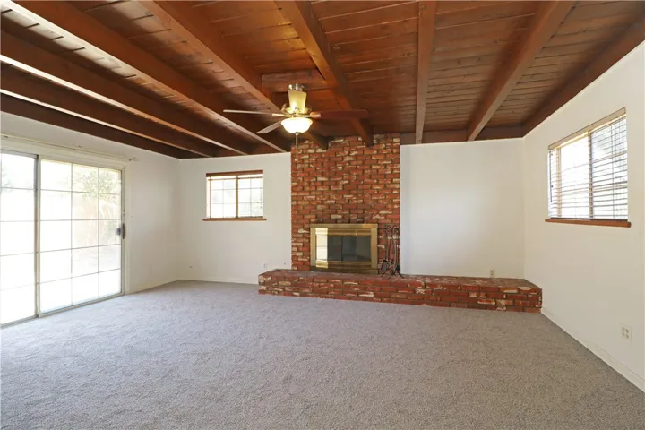 Spacious living room with exposed wood beams, brick fireplace and new carpet.