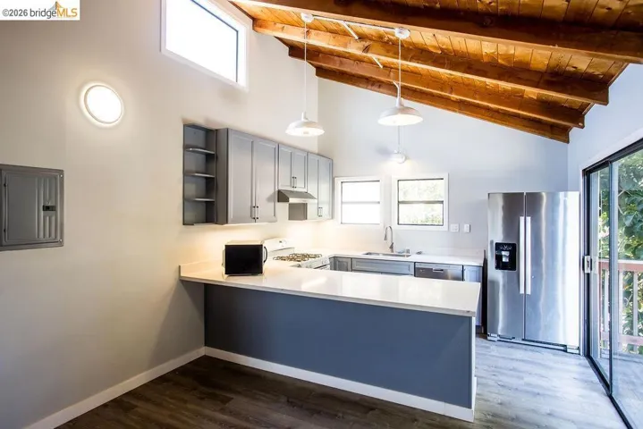 Kitchen featuring a vaulted wood-finish ceiling, gray cabinetry, stainless steel appliances, a white countertop island, and wood-finish flooring