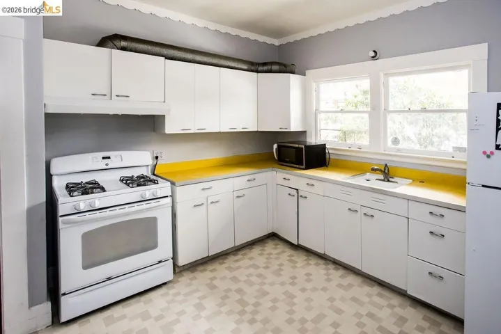 Kitchen featuring white cabinetry with brushed nickel hardware, a white gas range, and a dual-basin sink