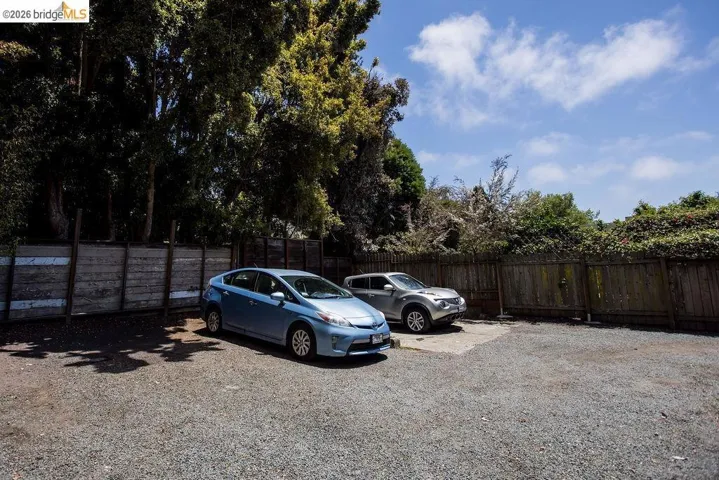 Gravel parking area featuring a wooden plank fence and mature trees